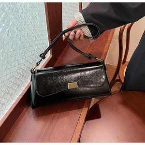 Detail of black pleated rectangular underarm bag with gold buckle on wooden windowsill