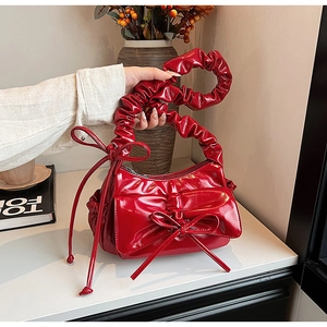 Détail d'un sac à main en cuir verni rouge avec anse plissée et nœuds décoratifs