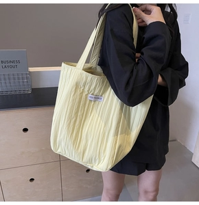 Close-up of light yellow pleated tote bag showing fabric texture and white logo patch