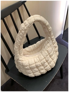Detailed close-up of quilted cream puffy bag with soft texture on a black wooden chair