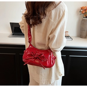 Détail d'un sac à épaule en cuir verni rouge avec un grand nœud décoratif au dos