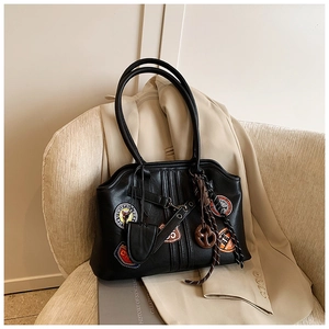 Gros plan détaillé des badges rétro sur un grand sac cabas noir posé sur une chaise en tissu