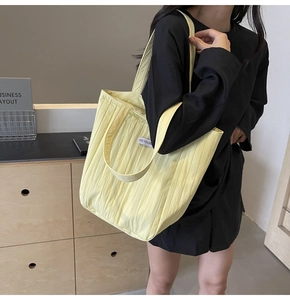 Detail of light yellow pleated tote bag showing the textured fabric and brand label