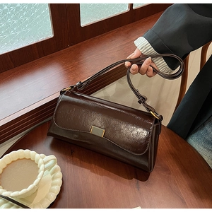 Detail of a dark brown glossy leather baguette bag with a gold metal clasp on a wooden table