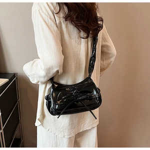 Détail du sac à épaule noir en similicuir brillant avec nœud élégant et bandoulière plissée