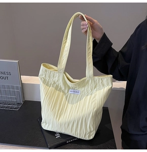 Detail of light yellow pleated canvas tote bag with black Kiss Yourself logo label