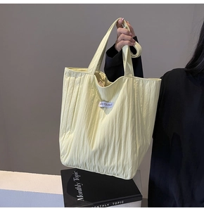Detail of light yellow pleated tote bag showing the vertical texture and brand tag
