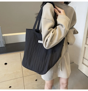 Close-up of black pleated tote bag with Kiss Yous label and reinforced shoulder strap