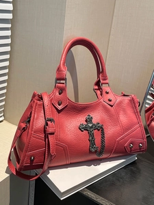 Red pebbled leather gothic crossbody bag with metallic cross and rivets on a white pedestal
