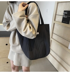 Detail of black pleated tote bag showing fabric texture and a white brand label