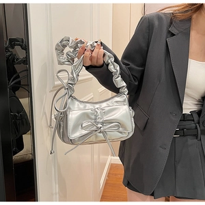 Détail du sac argenté en PU avec poignée plissée et grand nœud métallique décoratif