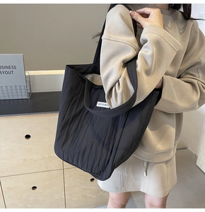Close-up of black pleated tote bag with Kiss Yourself label on lightweight fabric
