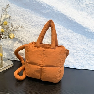 Sac fourre-tout matelassé orange vif en duvet avec bandoulière sur table en bois
