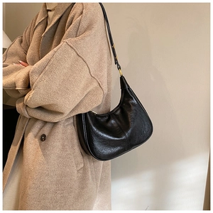Close-up of elegant black crescent leather shoulder bag styled on a wool coat