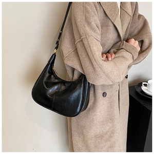 Close-up of a black crescent hobo bag with vintage texture and gold hardware on a coat