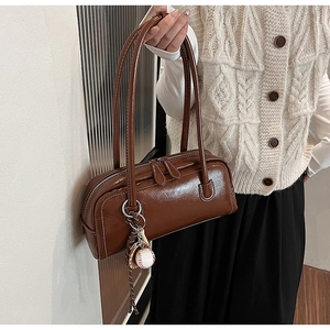 Detail of a brown leather baguette bag featuring white contrast stitching and baseball charm