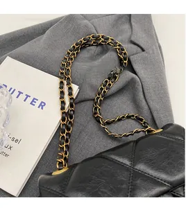 Détail du sac bandoulière matelassé noir avec chaîne dorée sur un blazer gris