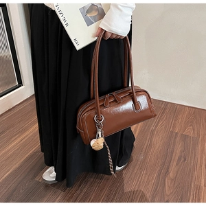 Detail of a brown glossy leather baguette bag with a cute bear charm in a natural setting