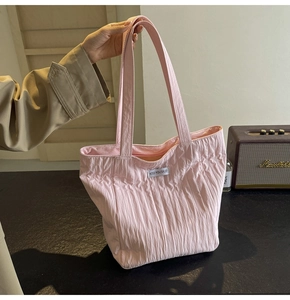 Detail of light pink pleated tote bag with Kiss Yourself patch shown in a lifestyle setting