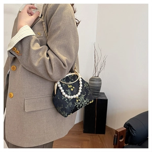 Detalle de elegante bolso bordado negro con asa de perlas y motivo de bambú