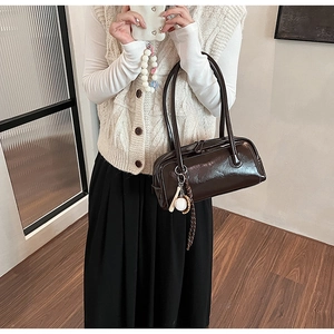 Detail of dark brown baguette bag in glossy patent leather with baseball charm