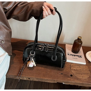 Detail of black patent leather baguette bag with white stitching and baseball charm