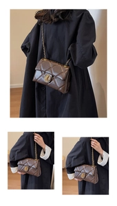 Sac bandoulière matelassé marron avec boucle lion dorée et chaîne sur un manteau
