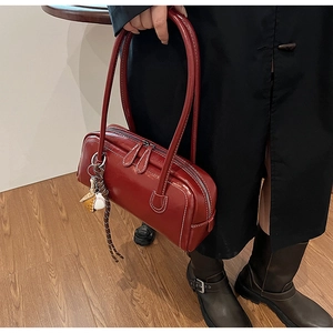 Detail of dark red vintage glossy leather Boston bag with baseball charm and long straps