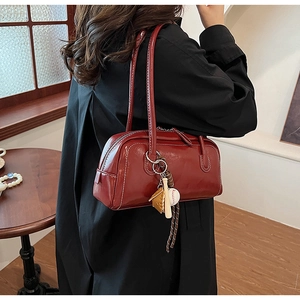 Detailed macro view of dark red glossy shoulder bag with white stitching and baseball charm