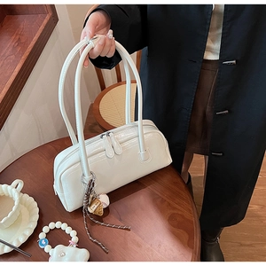 Detailed view of a white leather baguette bag with dual zippers and a baseball charm pendant