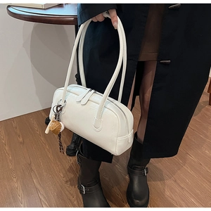 Detail view of a white patent leather baguette bag with a cute brown plush pendant accessory