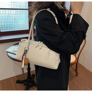 Polished white bowling bag styled with a black trench coat in a cozy cafe setting