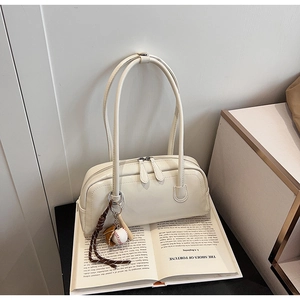 Close-up of cream leather baguette bag with baseball charm on a vintage prop book