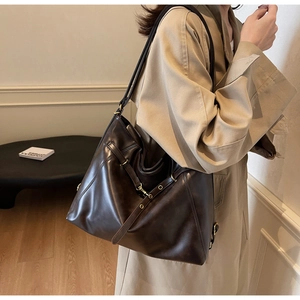 Detail of a large dark brown faux leather tote bag with gold buckle and long straps