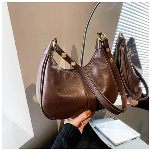 Detail of dark brown semi-circle hobo bag featuring glossy leather and gold studs