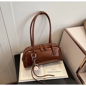 Detail view of coffee brown faux leather baguette bag with baseball charm and stitching