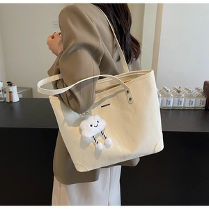 Detail of a large cream tote bag with soft cloud pendant on a model in a brown suit