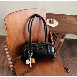 Detail of vintage black leather baguette bag with white contrast stitching and baseball charm