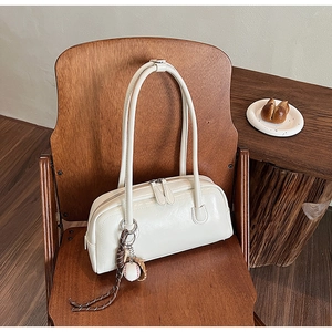 Detail of cream white faux leather baguette bag with baseball charm on a wooden chair