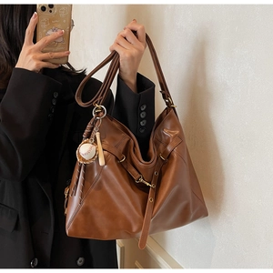 Macro detail of dark brown leather tote bag featuring a baseball charm and shoulder strap