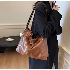 Close-up of brown leather tote bag featuring a cross buckle and baseball pendant charm