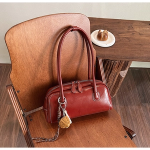 Close-up of vintage dark red baguette bag on a wooden chair with textured stitching and charm