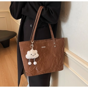 Detail of crinkled brown tote bag with a cute white cloud plush pendant for daily commute