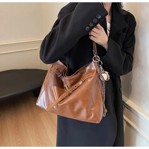 Detail of a large brown tote bag featuring a baseball charm and adjustable shoulder strap