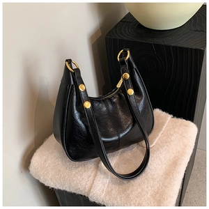 Detail of black leather half-moon bag with golden rivets and metallic ring details