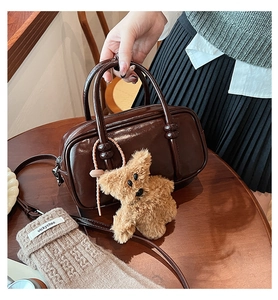 Dettaglio di una borsa bowling in ecopelle marrone lucida con ciondolo a forma di orso