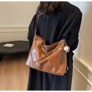 Detail of caramel brown large tote bag with baseball charm and gold hardware on model
