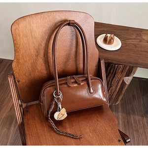 Detail view of a vintage brown leather shoulder bag with creative baseball charm and textures
