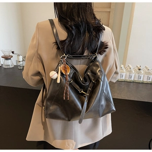 Detail of black leather tote bag showing smooth texture and baseball keychain accessory