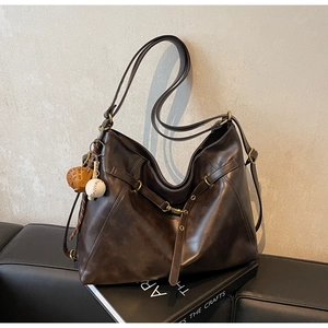 Detail view of large vintage brown leather tote bag with creative baseball charm on sofa